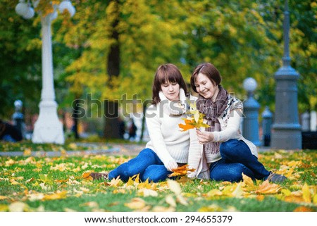 Mother and daughter together in park on a bright fall day, having fun and lying on the ground in autumn leaves