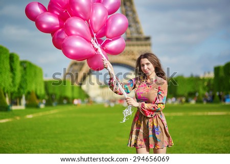 Happy young girl in colorful dress with huge bunch of pink balloons near the Eiffel tower in Paris