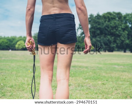 Rear view shot of athletic young woman walking in the park with a jump rope in her hand