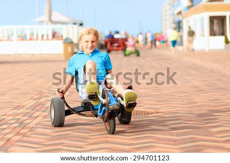 Happy kids enjoying active holidays on the beach. Sportive boy riding pedal car along the promenade on a summer day at sunset. 