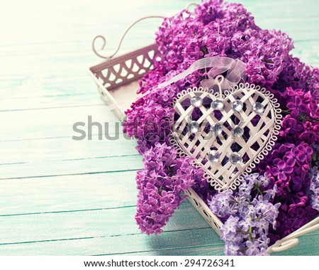 Background  wit  lilac flowers on tray  and  white decorative heart on turquoise painted wooden planks. Selective focus. Place for text. Toned image.
