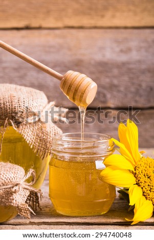 A jar of honey with sunflowers and spoon on old wooden backgroun