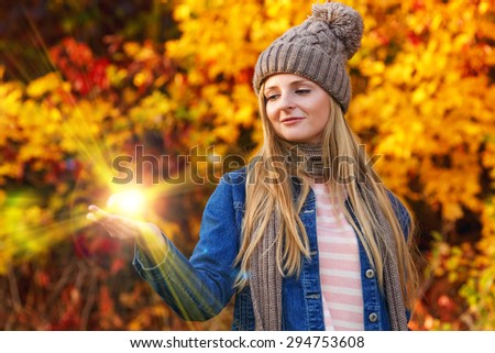 Woman is holding the sun. Bright rays of light energy in the hand of the beautiful woman in autumn hat. Sun's rays in hand. Autumn, nature, park, woman - the concept of health and beauty.
