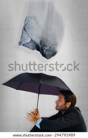 Businessman holding umbrella sitting on the floor against grey room