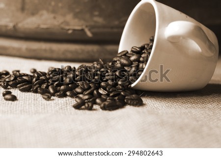 sepia color style picture of coffee bean flowing from coffee cup on jute cloth 