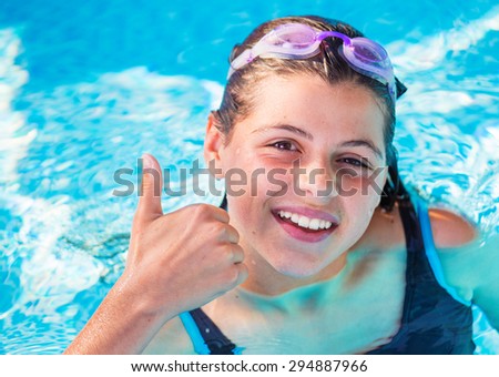 smiling girl in a pool with pink swimming goggles with the thumbs up