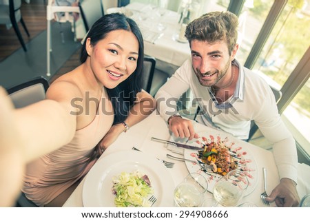 Couple of lovers in a restaurant and taking a picture - Romantic date in a classy restaurant at sunset - Two attractive friends having fun in a bistro bar