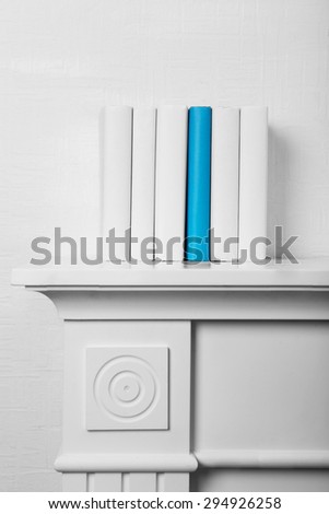 Blank books and one blue on shelf on white wallpaper background