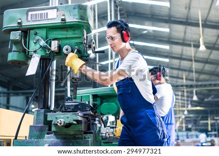 Asian worker in production plant drilling at machine on the factory floor
