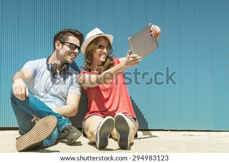 summer holidays, teenage and technology concept - couple of smiling teenagers in sunglasses taking selfie with tablet pc