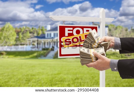 Man Handing Over Thousands of Dollars in Front of House and Sold For Sale Real Estate Sign.