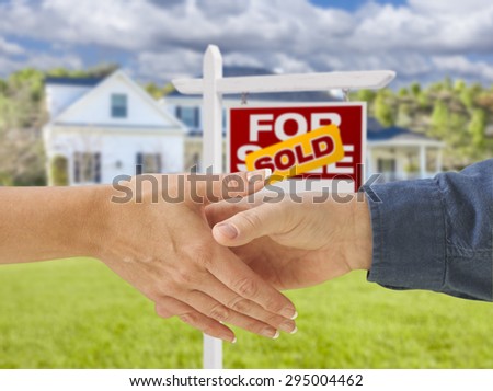 Man and Woman Shaking Hands in Front of a Beautiful New House and Sold For Sale Real Estate Sign.
