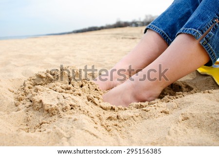 Picture of female feet buried in sand at the beach.
