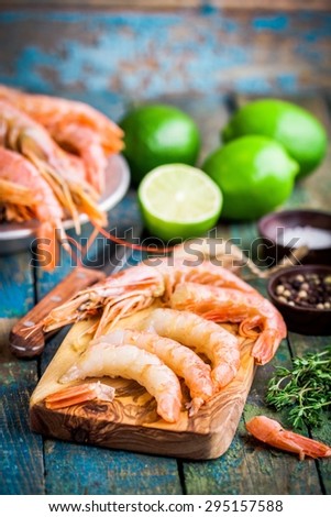 peeled raw prawns on a wooden cutting board with salt, pepper, lime on a rustic table