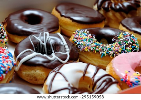 Picture of assorted donuts in a box with chocolate frosted, pink glazed and sprinkles donuts. Royalty-Free Stock Photo #295159058