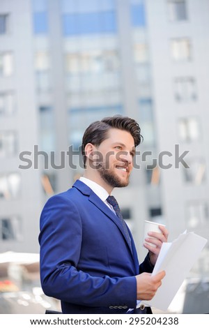 Good worker. Vivacious nice bearded businessman smiling and holding papers while drinking coffee.