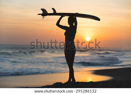 Beautiful young surfer girl in bikini with surfboard on a beach