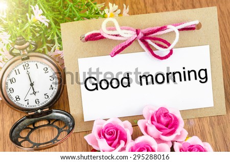 Good morning paper tag and pocket watch with pink rose on wooden background.