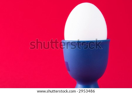 A white egg in a blue egg cup with a red background