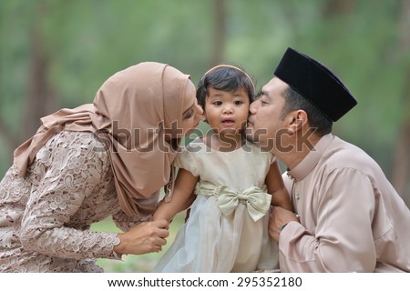malay family having fun in the park ,malaysian people. Mother and father kissing his daughter. Royalty-Free Stock Photo #295352180