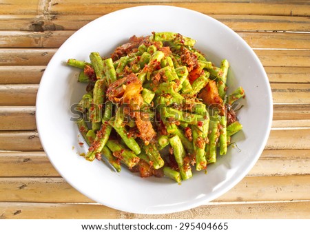 Stir fried crispy pork belly and red curry paste with string bean in white dish on wood background