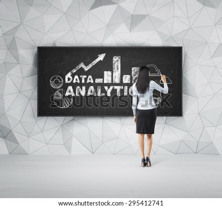 Rear view of full-length brunette woman who is presenting analytical solutions on the black board.