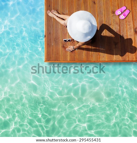 Summer holiday fashion concept - tanning woman wearing sun hat at the pool on a wooden pier shot from above