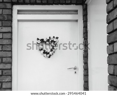 Wedding (or birth) flower wreath in heart shape on door. London, UK. Aged photo. Black and white..