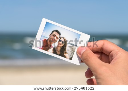 Man Hand Holding Instant Photo Of Young Happy Couple, focus on hand