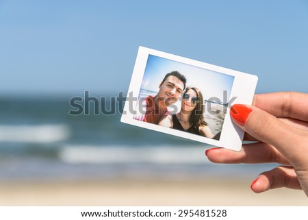 Girl Hand Holding Instant Photo Of Young Happy Couple, focus on hand
