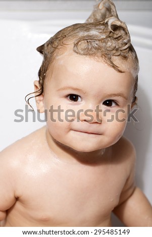 One small beautiful male child with wet hair sitting in bathroom smiling looking forward on white background, vertical picture