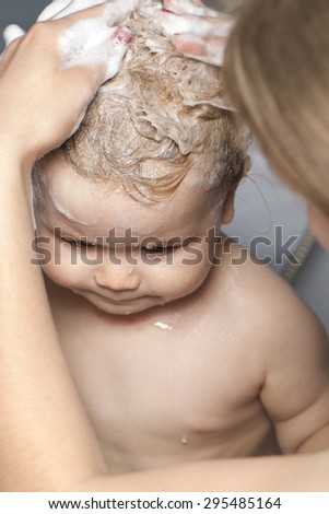 Little cute wet baby boy taking shower washing hair foam soap with help of mother in bath room closeup, vertical picture