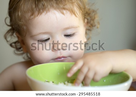 Portrait of little male kid with blonde curly hair and round cheecks eating from green plate with hand closeup, horizontal picture