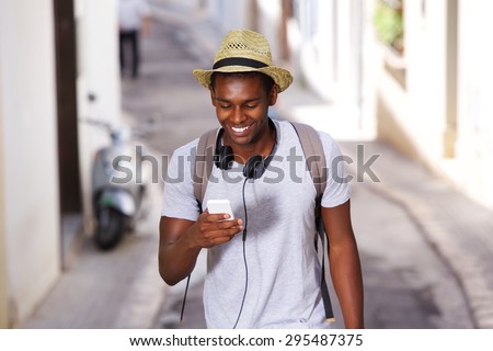 Portrait of a happy young african american man walking in town with mobile phone