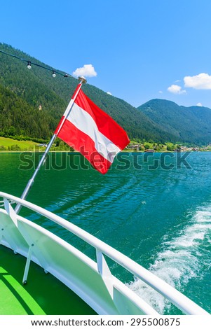 Austrian flag waving on the wind during ship cruise on green water Weissensee lake, Austria