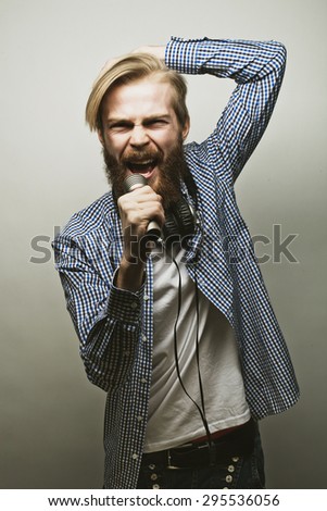 Life style concept: a young man with a beard wearing a white shirt holding a microphone and singing. Over gray background.