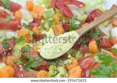 Seasoning in a wooden spoon on top of the vegetable salad with tomato,cucumber,parsley,carrot,paprika and onions