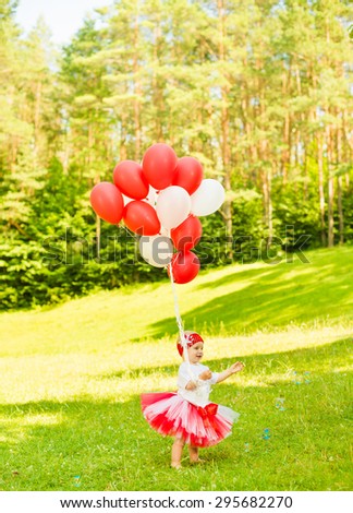 little girl in colorful dress with balloons at summer forest grass