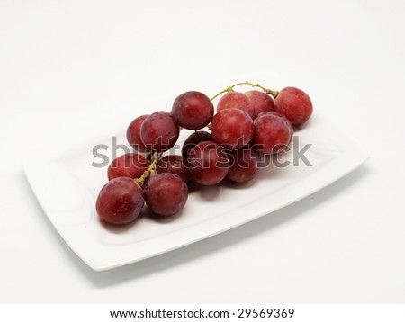 Red grapes on plate isolated over white background .