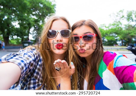 Close up lifestyle selfie portrait of pretty fresh young brunette and blonde best friends girls making selfie,having fun,sending kisses,wearing sunglasses. Fresh make-up,teenage outfit,summer vacation
