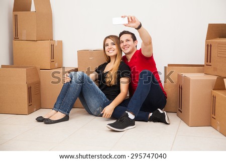 Cute married young couple having fun while moving to their new home and taking a selfie