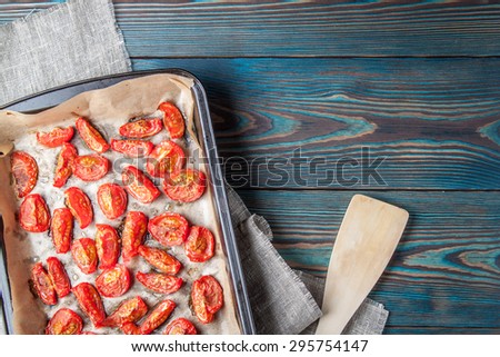 Dried tomatoes in baking tray and spatula on blue wooden background