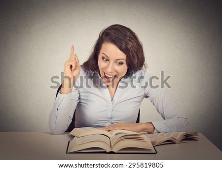 Smiling excited young woman reading a book has an idea pointing with finger up  Royalty-Free Stock Photo #295819805