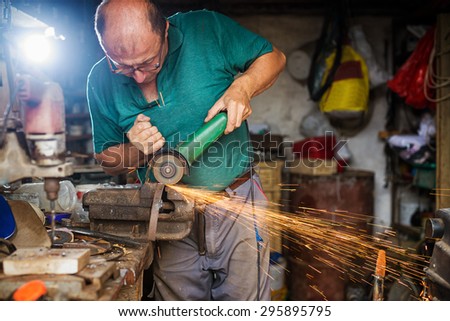 Craftsman sawing metal with disk grinder in workshop.