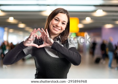 Young pretty girl make a heart with her hands on unfocused background