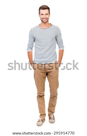 Confident and stylish. Full length of cheerful young man holding hands in pockets and looking at camera while standing against white background
