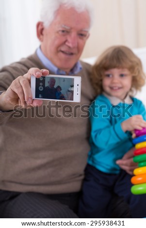 Aged smiling man doing selfie with cute grandson
