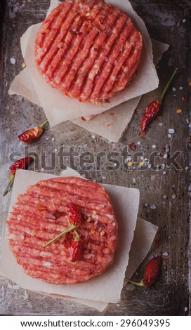 Raw Ground beef meat Burger steak cutlets with seasoning on vintage metal tray, black background, top view