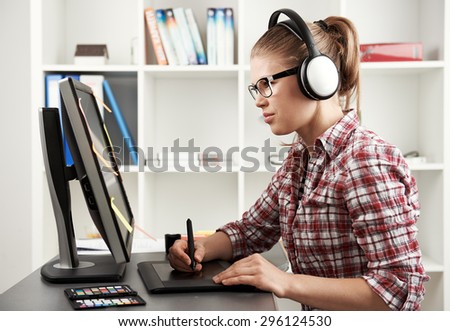 Female photographer editing illustration working with color palette at computer. Young graphic designer in headphones looking at monitor. 