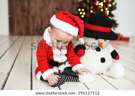 Little baby boy in santa suit on the floor with snowman near xmas tree